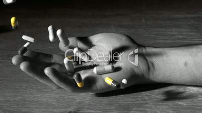 Mans hand falling holding pills after overdose in selective black and white