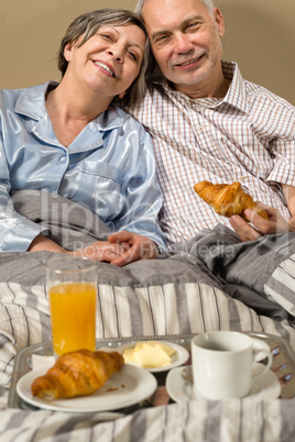 Happy retired couple eating croissant breakfast