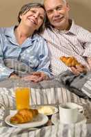 Happy retired couple eating croissant breakfast