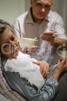 Mature man helping ill wife feeding soup