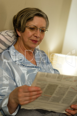 Relaxed smiling mature woman reading newspaper