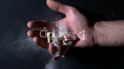 Hand holding white powder and pills dropping dead