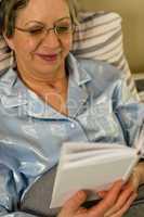 Elderly woman reading book lying in bed