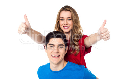 Joyous woman enjoying piggy ride and showing double thumbs up