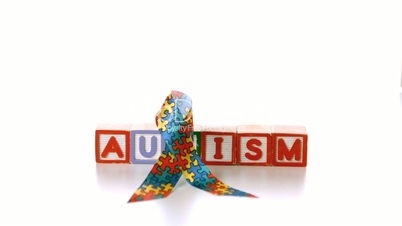 Awareness ribbon falling onto blocks spelling autism on white background