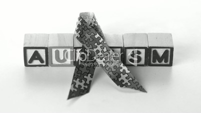 Awareness ribbon falling in front of autism letter blocks in black and white