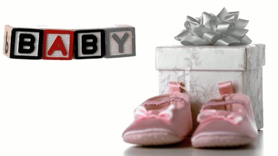 Blocks spelling baby falling beside booties and gift box