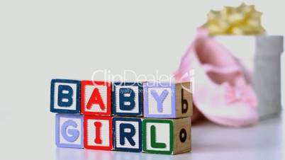 Baby girl blocks sliding across with booties and gift box in background