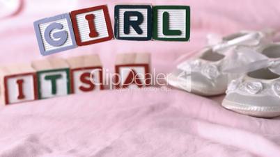 Its a girl message in letter blocks beside booties on pink blanket