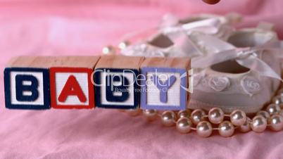Baby in letter blocks beside booties and pearls on pink blanket