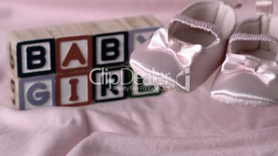 Baby booties falling on pink blanket with baby girl message in blocks