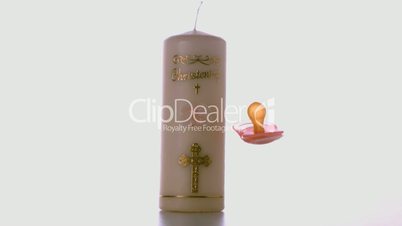 Pink pacifier falling beside baptism candle