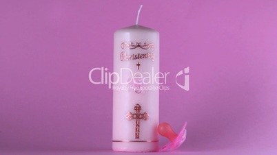 Pink pacifier falling beside baptism candle on pink background