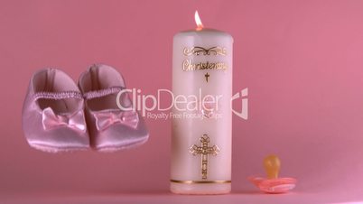 Baby shoes falling beside lit baptism candle and pacifier