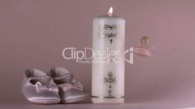 Pacifier falling beside lit baptism candle and baby shoes