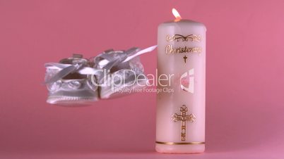 Baby shoes falling beside lit baptism candle