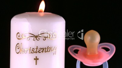 Pacifier falling beside lit baptism candle