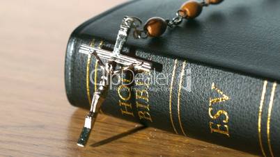 Rosary beads falling onto bible on a table