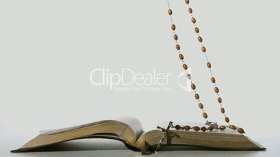 Rosary beads falling onto open bible on white background