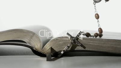 Rosary beads falling onto open bible on white background close up