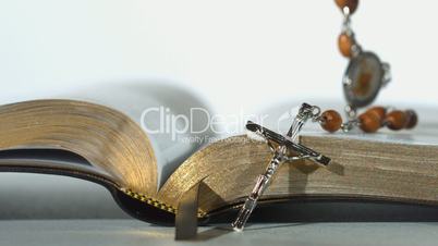 Rosary beads falling on open bible on white background close up