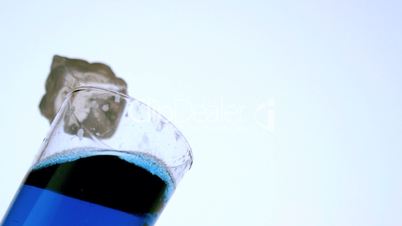 Ice falling and missing the glass of blue liquid