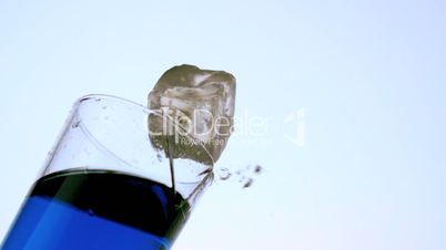 Ice falling and breaking glass of blue liquid