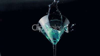 Ice falling into cocktail glass of blue liquid low angle