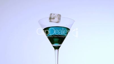 Ice falling into cocktail glass of blue liquid on white background