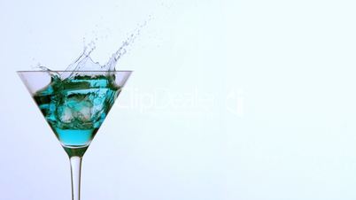 Ice falling into cocktail glass of blue alcohol on white background