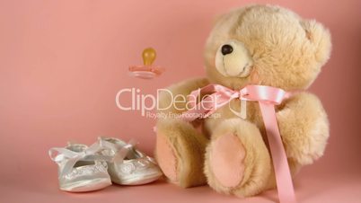 Pink soother falling onto a teddy bear and baby shoes