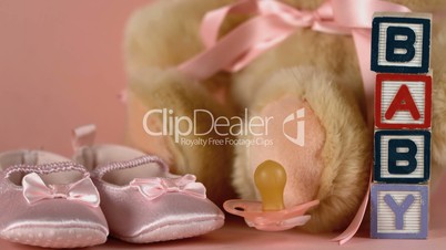 Pink soother falling besides baby shoes blocks and teddy bear