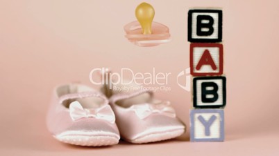 Pink soother falling in front of baby shoes and baby blocks