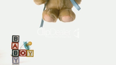 Teddy bear falling besides baby blocks and blue soother