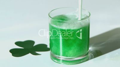 Green beer pouring into tumbler beside paper shamrock