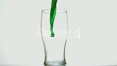 Green beer pouring into a pint glass on white background