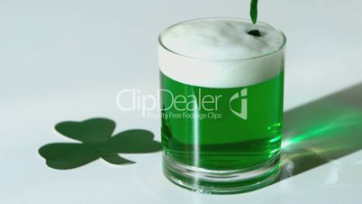 Green beer pouring into a tumbler beside paper shamrock