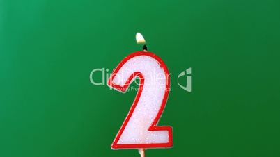 Two birthday candle flickering and extinguishing on green background