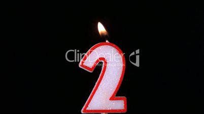 Two birthday candle flickering and extinguishing on black background