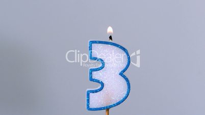 Three birthday candle flickering and extinguishing on blue background
