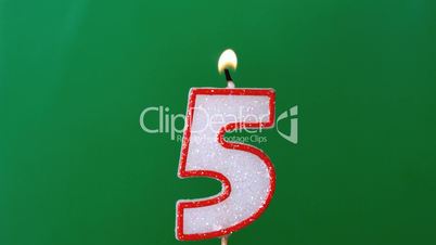 Five birthday candle flickering and extinguishing on green background