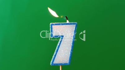 Seven birthday candle flickering and extinguishing on green background