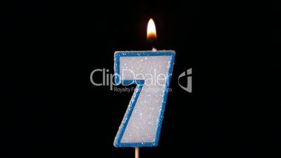 Seven birthday candle flickering and extinguishing on black background