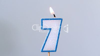 Seven birthday candle flickering and extinguishing on blue background