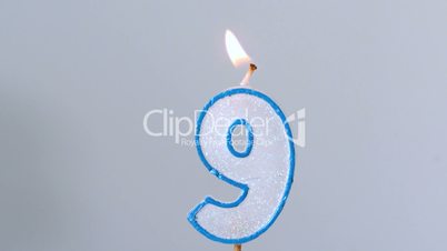 Nine birthday candle flickering and extinguishing on blue background