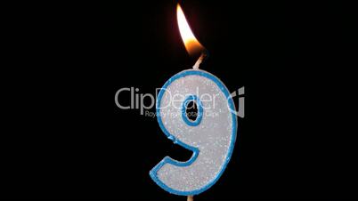 Nine birthday candle flickering and extinguishing on black background