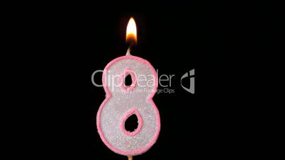 Eight birthday candle flickering and extinguishing on black background