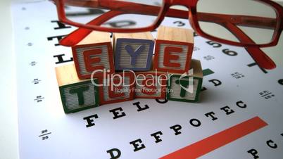 Glasses falling onto eye test with blocks spelling out eye test