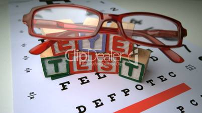 Glasses falling onto eye test with wooden blocks spelling out eye test