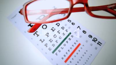 Red reading glasses falling onto an eye test overhead shot
